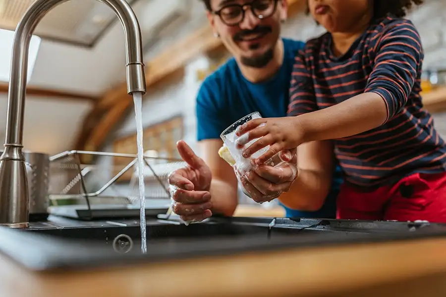 father and young daughter washing dishes together, clean water coming from faucet at kitchen sink - Springfield, IL